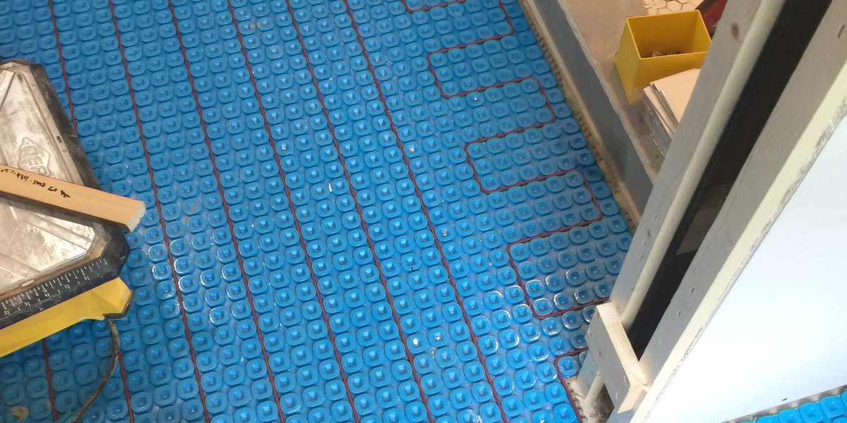 Floor heating sensor probe embedded between electric heating cables inside a blue uncoupling membrane.