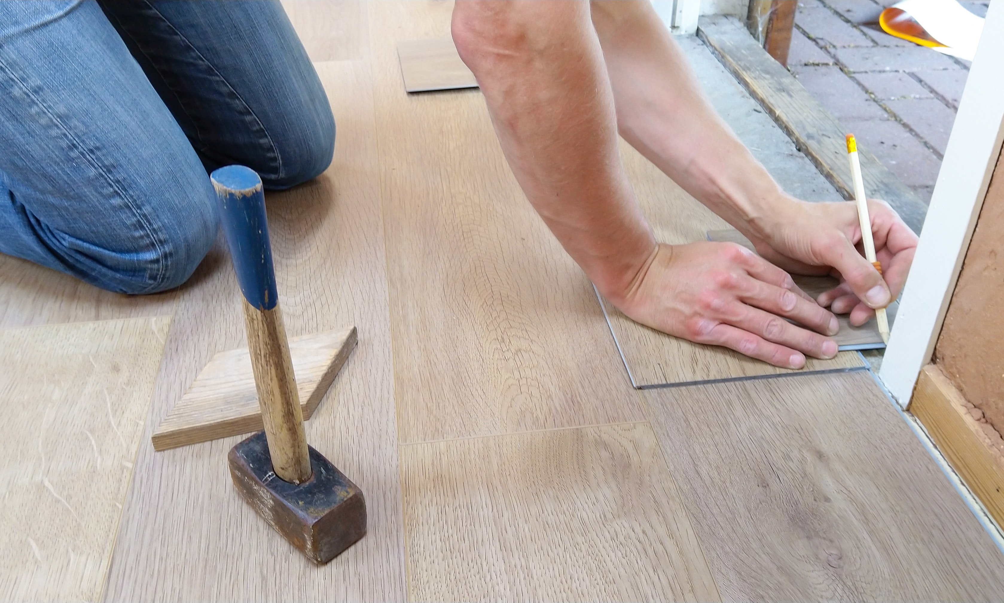 An installer marks a luxury vinyl plank for cutting near a doorway while installing new flooring.