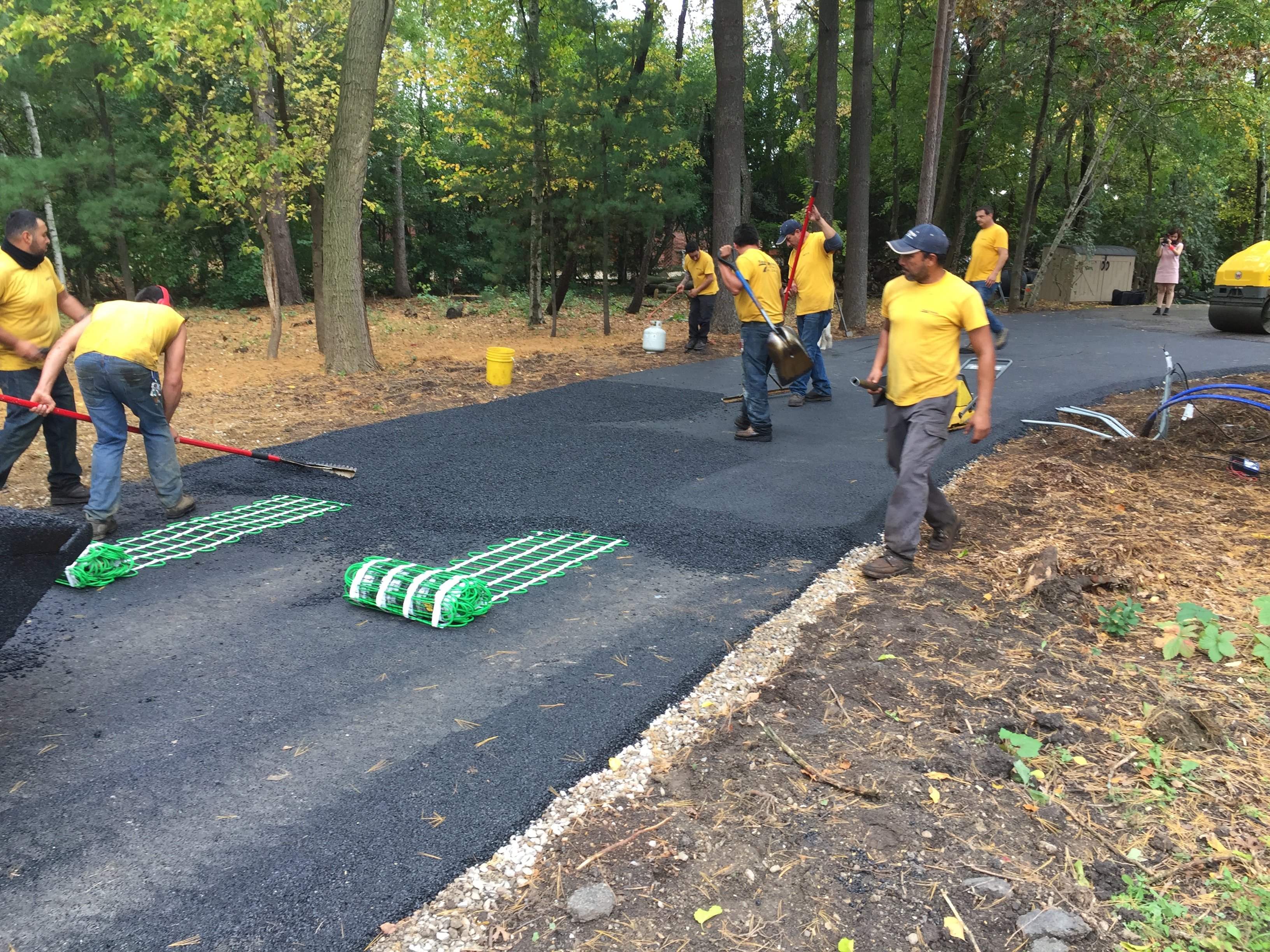 Work crew installing snow melting mats with green heating cable on a driveway before applying a layer of fresh asphalt.