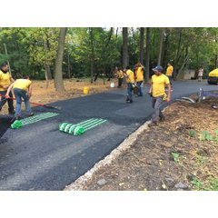 Work crew installing snow melting mats with green heating cable on a driveway before applying a layer of fresh asphalt.