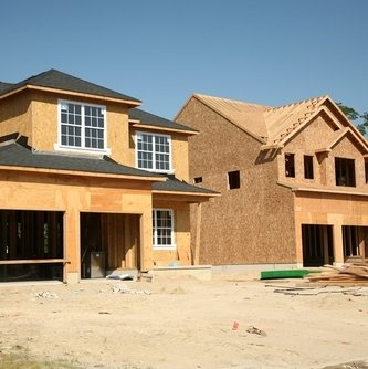 Multiple two-story single-family homes under construction with wood framing and sheathing in a residential subdivision.