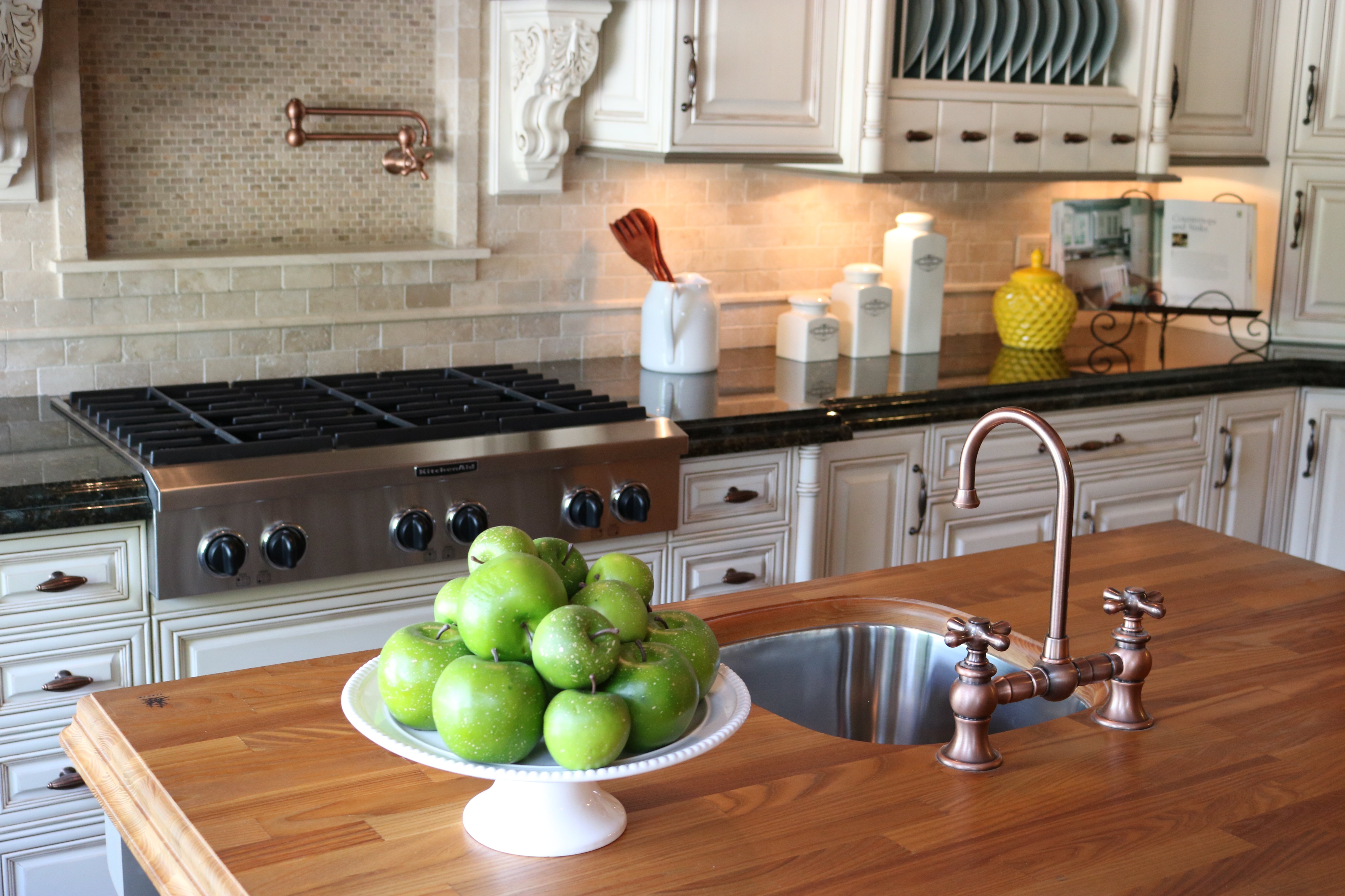 A traditional kitchen featuring a butcher block island with a stainless steel sink and KitchenAid appliances set against off-white cabinetry.