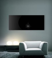 A modern black glass LAVA radiant heating panel with a decorative crystal design mounted on a light grey living room wall.