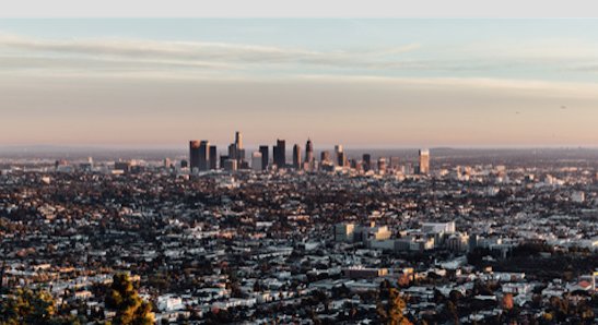 Panoramic view of the Los Angeles skyline and metropolitan basin under a pastel sunset.