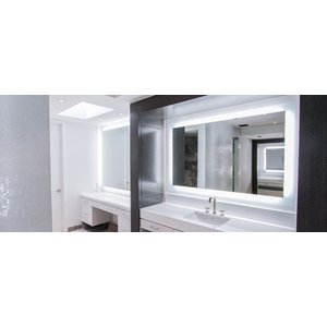 A modern bathroom featuring a Clara LED backlit mirror with a glowing frosted perimeter mounted above a white vanity with a chrome faucet.