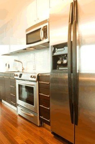 A modern kitchen interior with stainless steel appliances, dark wood cabinetry, and glossy hardwood flooring.
