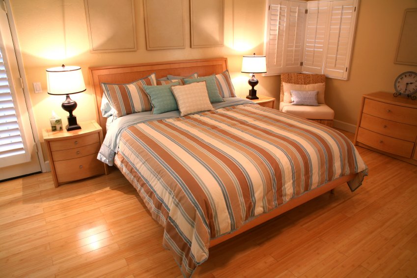 A modern master bedroom interior featuring light-toned wood flooring and a bed with a striped comforter.