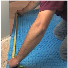 A person measuring a blue Prodeso uncoupling membrane installed on a subfloor for an electric radiant floor heating system.