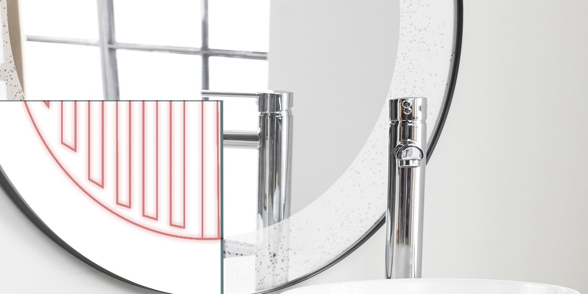A mirror defogger installed behind a round bathroom mirror, illustrated by a red heating cable pattern overlay to demonstrate how the electric radiant heating system prevents condensation.
