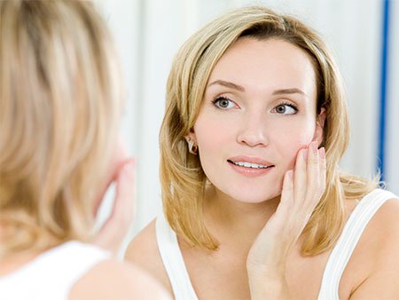 A woman looking into a clear, fog-free bathroom mirror during a skincare routine, enabled by a mirror defogger.