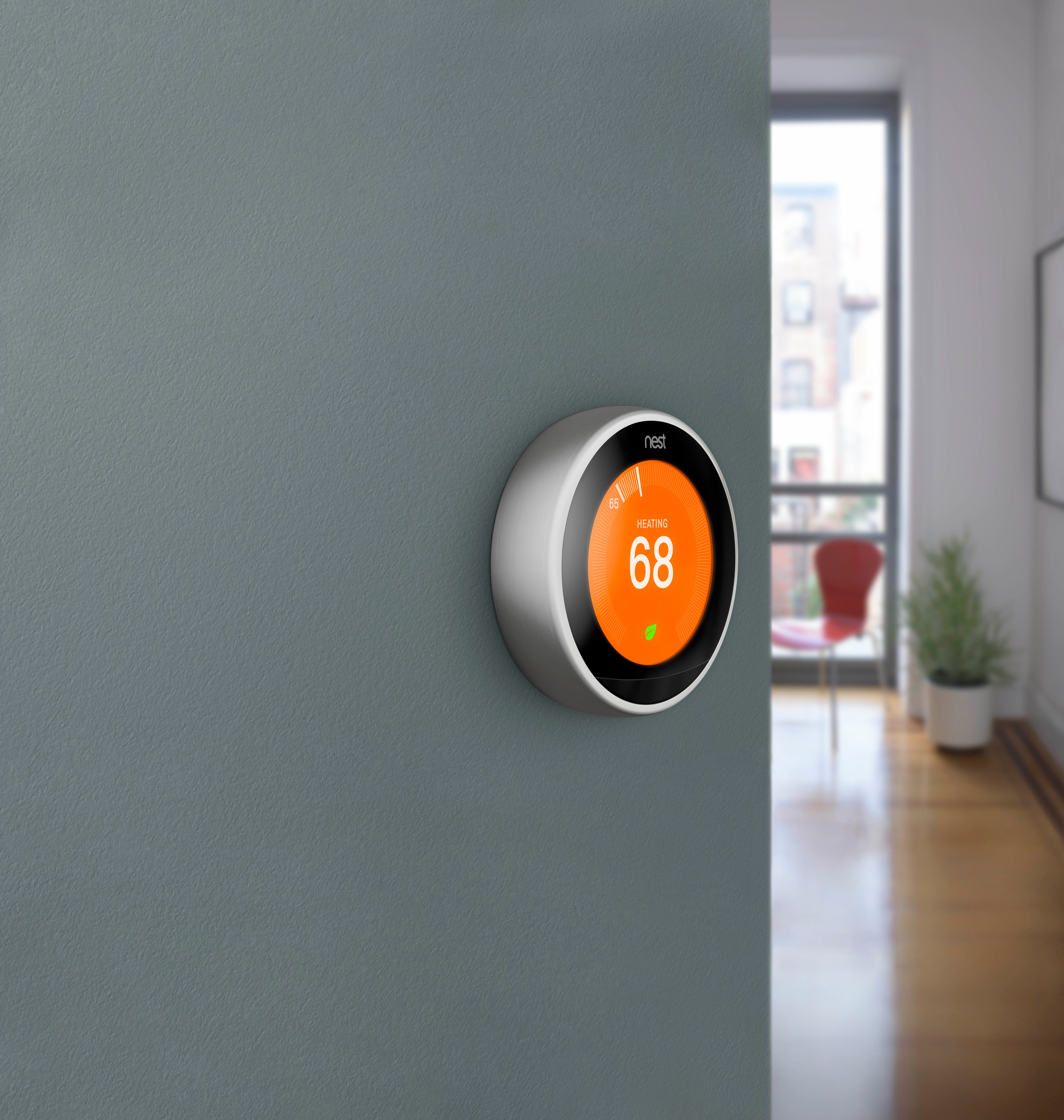 A Nest Learning Thermostat mounted on a grey wall displaying an orange heating screen set to 68 degrees for electric radiant floor heating.
