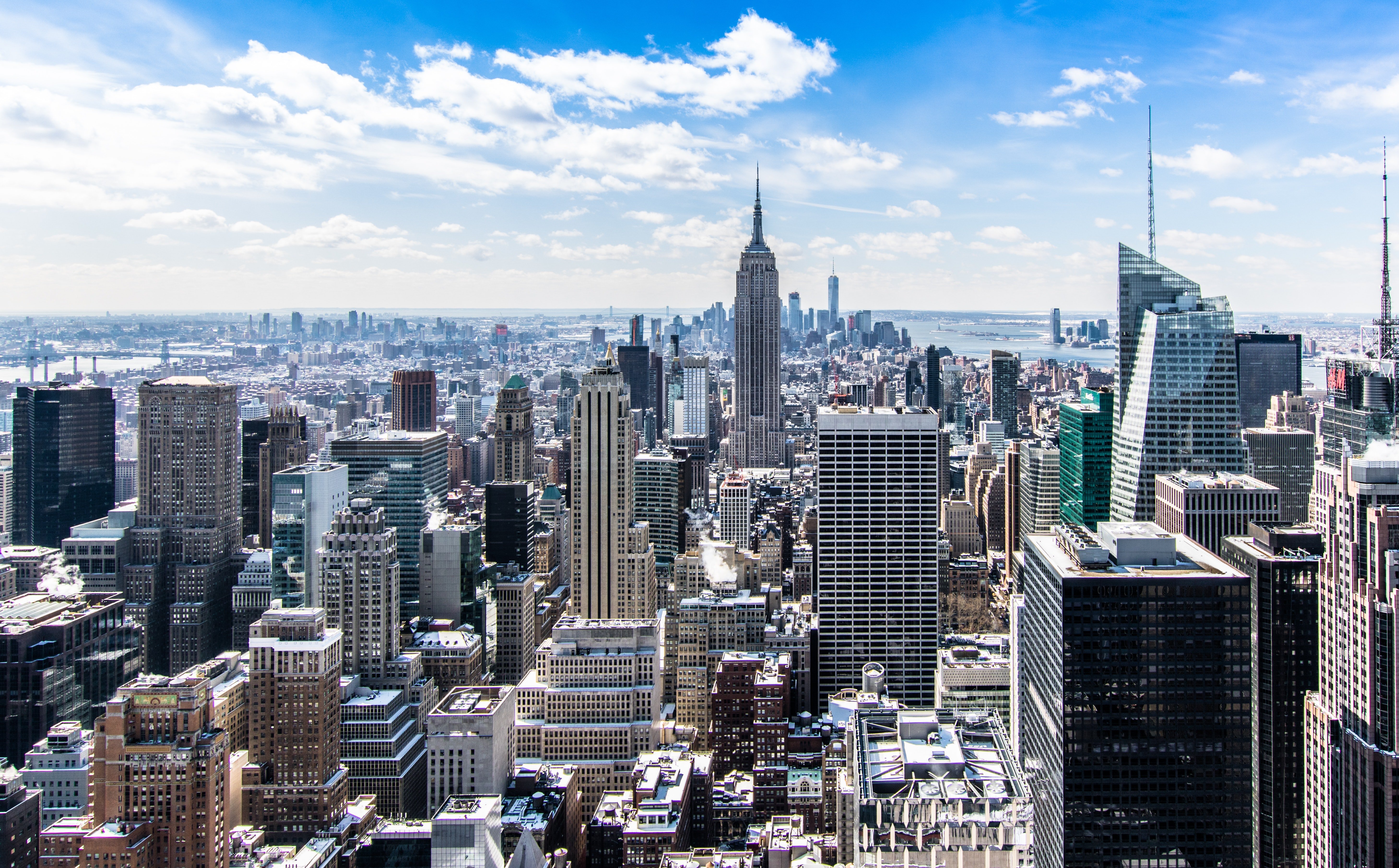 Aerial view of the Midtown Manhattan skyline featuring the Empire State Building and snow-dusted rooftops under a clear blue sky.