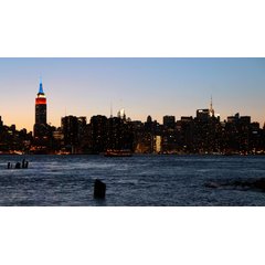 The New York City skyline at dusk featuring the Empire State Building and Chrysler Building illuminated above dark water.