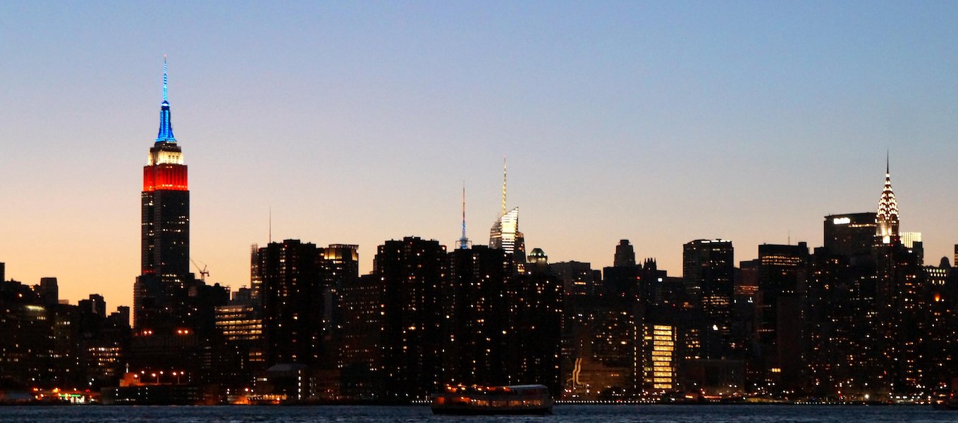 The New York City skyline at dusk featuring the illuminated Empire State Building, Bank of America Tower, and Chrysler Building.