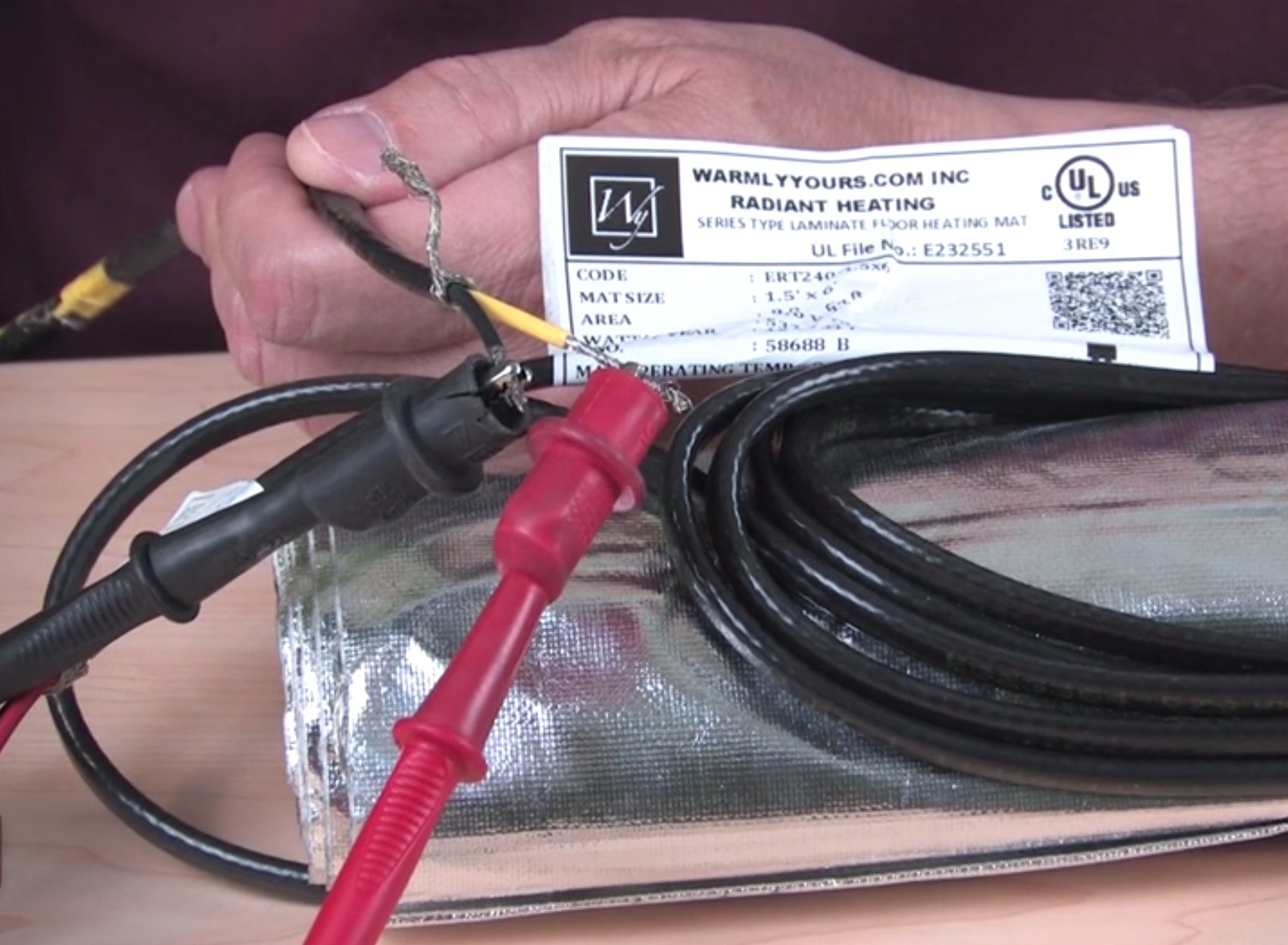 A technician uses a multimeter to test the electrical resistance of a WarmlyYours Environ electric radiant floor heating mat.
