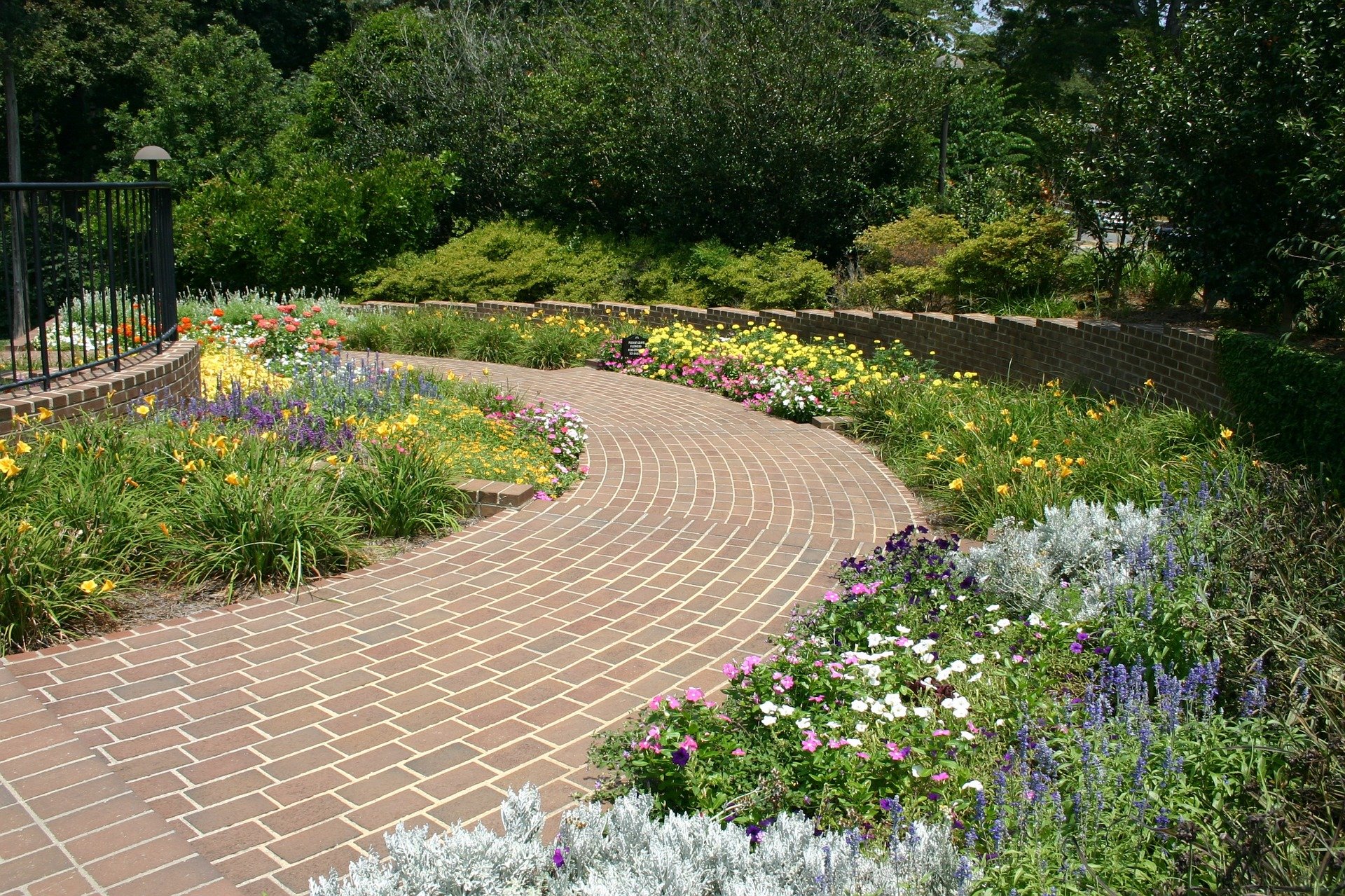 A curving brick paver walkway lined with vibrant flower beds and a low retaining wall in a landscaped garden.