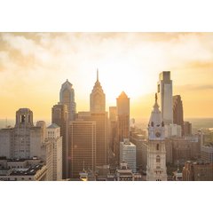 The Philadelphia skyline at sunrise with golden light illuminating One Liberty Place, the Comcast Center, and the City Hall clock tower.