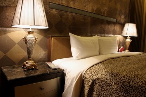 A cozy hotel-style guest bedroom with a bed, marble-topped nightstands, and warm accent lighting.