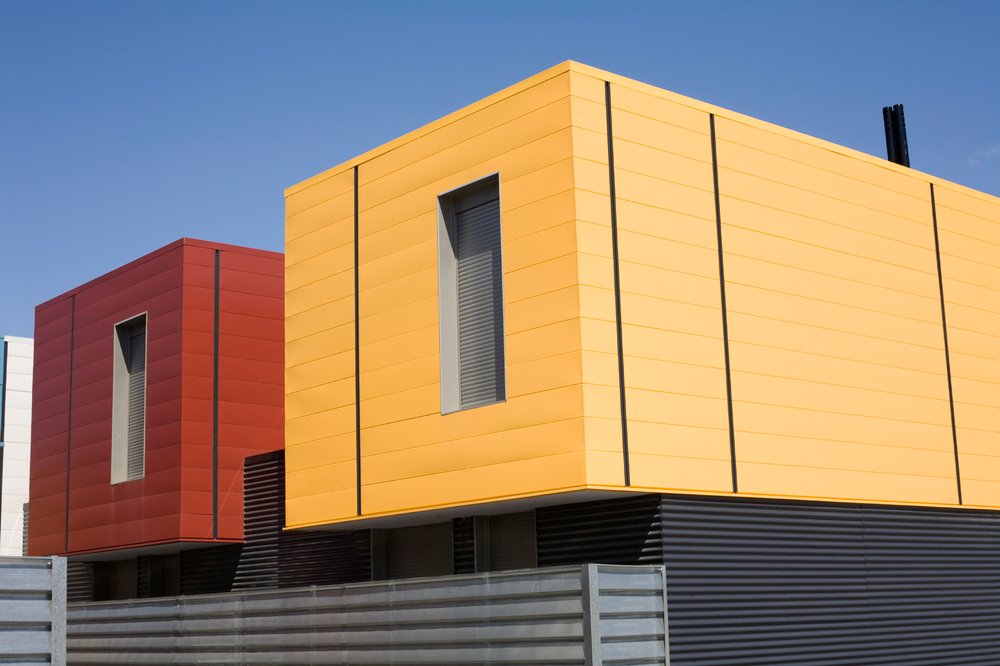Modern prefabricated homes with yellow and red exterior paneling designed for energy-efficient radiant heating.