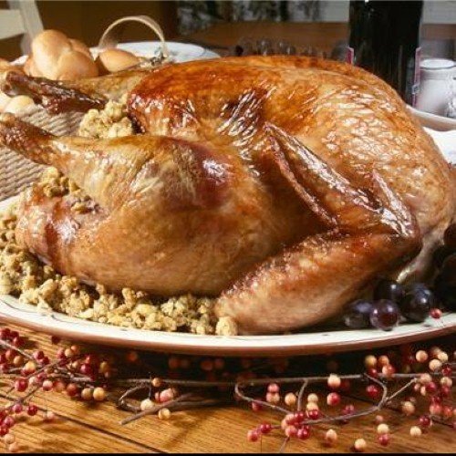 A golden-brown roasted turkey served on a platter with stuffing and grapes on a festive dining table.