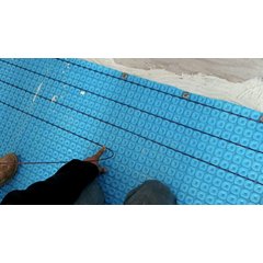 A red TempZone heating cable being installed into a blue Prodeso uncoupling membrane for an electric radiant floor heating system.