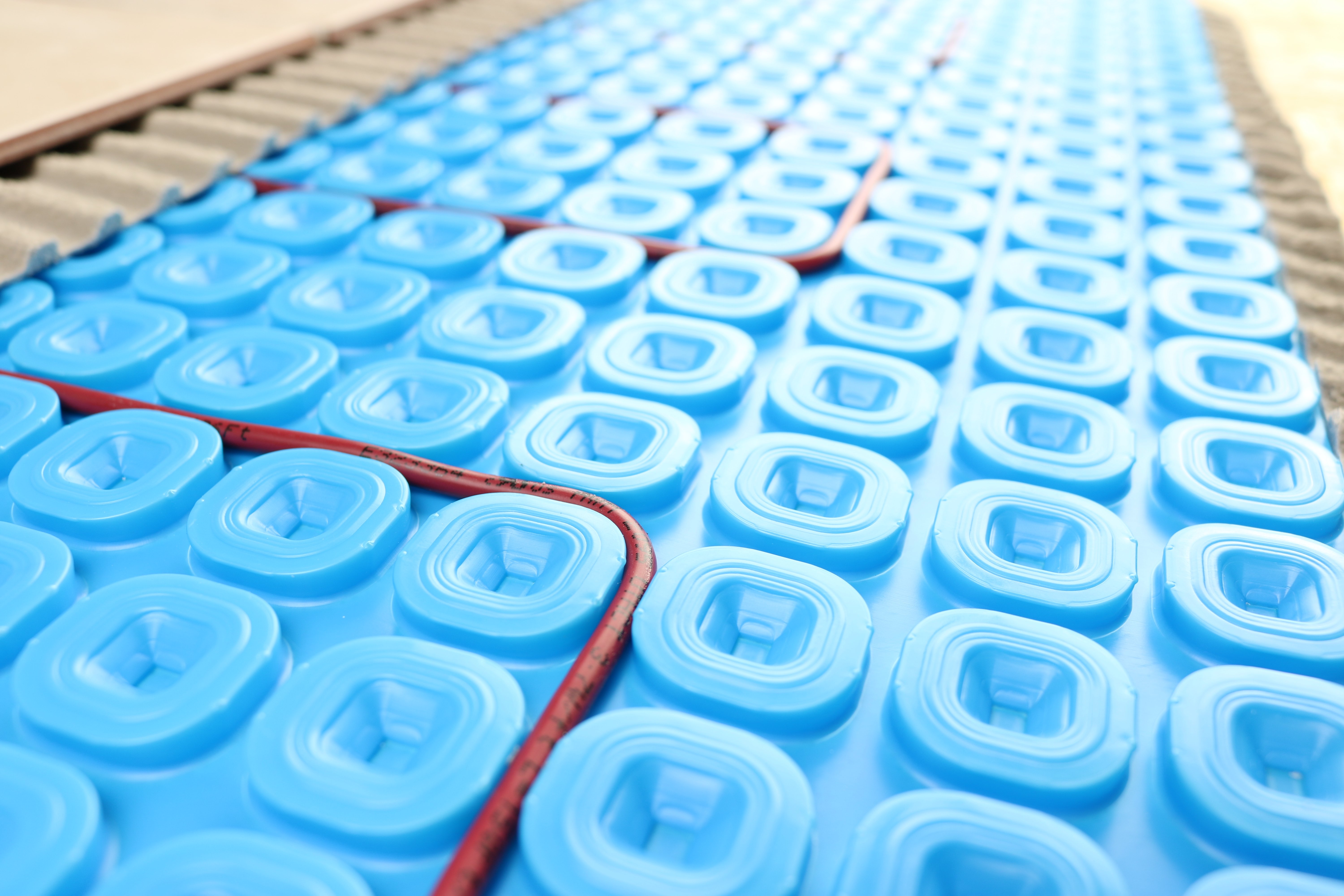 A TempZone heating cable routed in a serpentine pattern within a blue Prodeso uncoupling membrane for electric radiant floor heating.