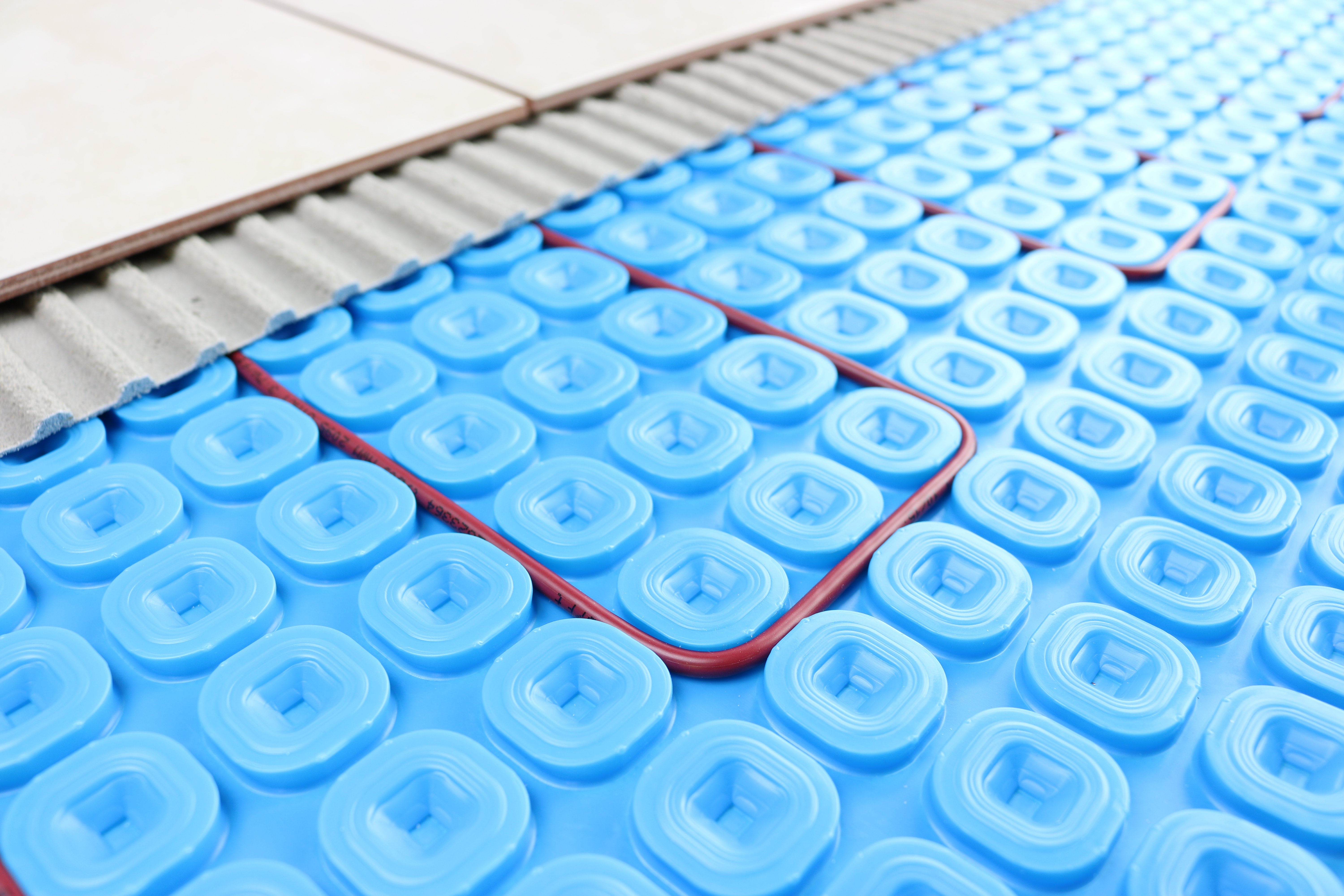 TempZone heating cable installed in a blue Prodeso uncoupling membrane beneath thinset mortar and ceramic floor tiles.