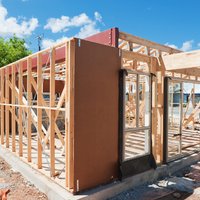 Residential building under construction with timber framing, a red steel I-beam header, and concrete slab foundation.