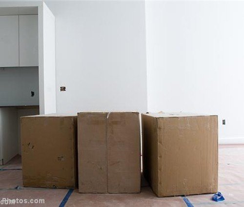 Three sealed cardboard boxes containing electric radiant floor heating components staged on a floor during a home renovation.