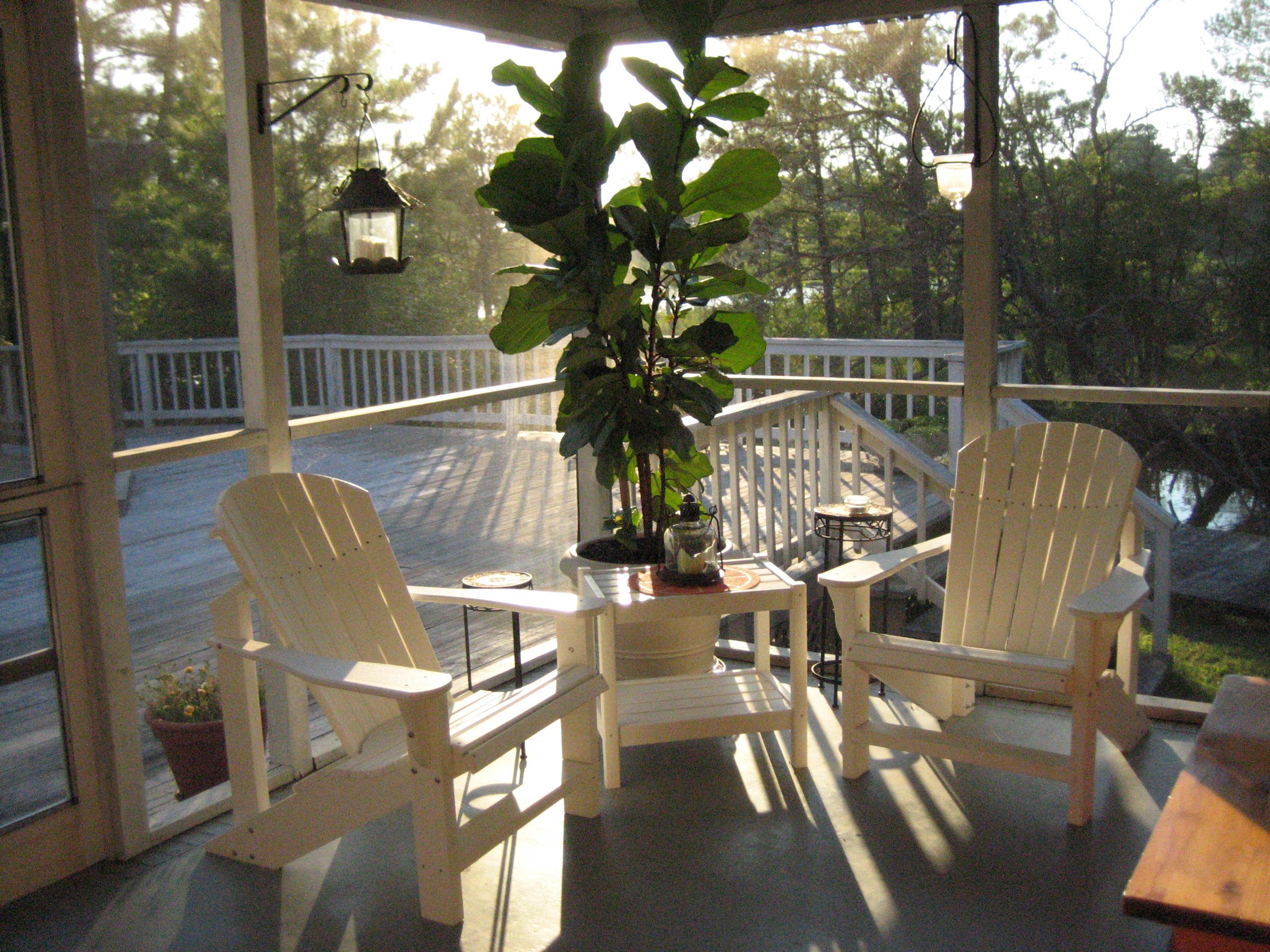 A sunlit screened-in porch featuring electric radiant floor heating beneath a smooth grey finished floor with Adirondack chairs.