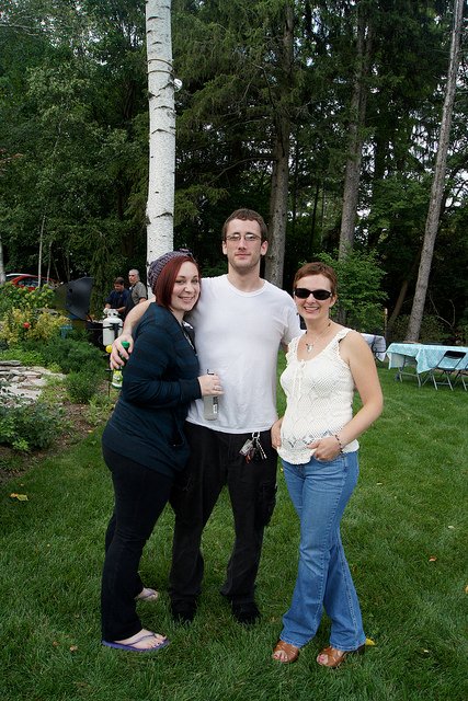 Three people standing together on a backyard lawn surrounded by trees and garden beds in memory of Mason Prideaux.