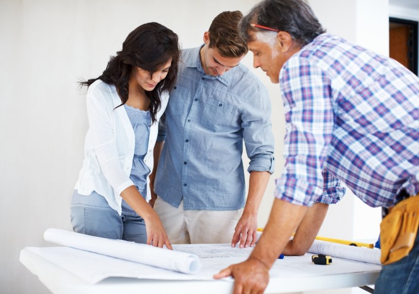 A contractor reviewing architectural blueprints with a couple during a home remodeling project.