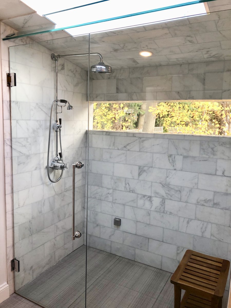 “Walk-in shower with white marble wall tile, glass door, and linear drain accenting heated floors.”
