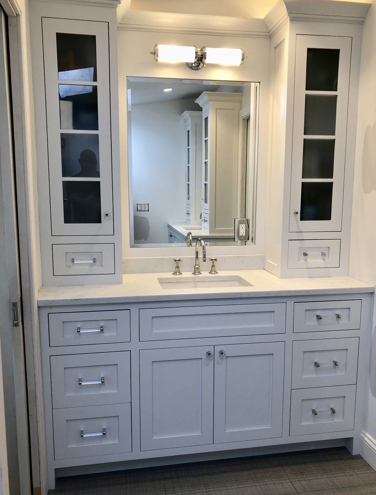 “White bathroom vanity flanked by built-in cabinets over newly installed grey radiant heated tile flooring.”