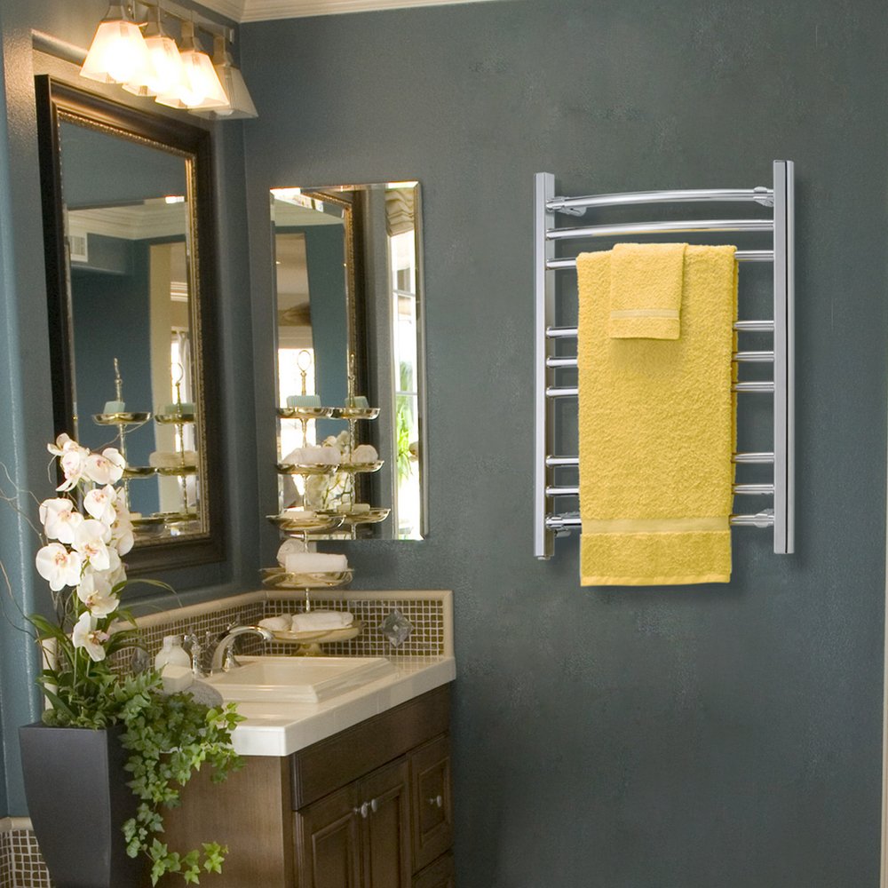 A Riviera towel warmer with a polished metallic finish mounted on a dark grey-green bathroom wall, holding draped yellow bath and hand towels.