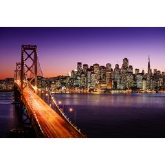The San Francisco skyline and Bay Bridge illuminated at night with traffic light trails crossing the suspension span under a dusk sky.