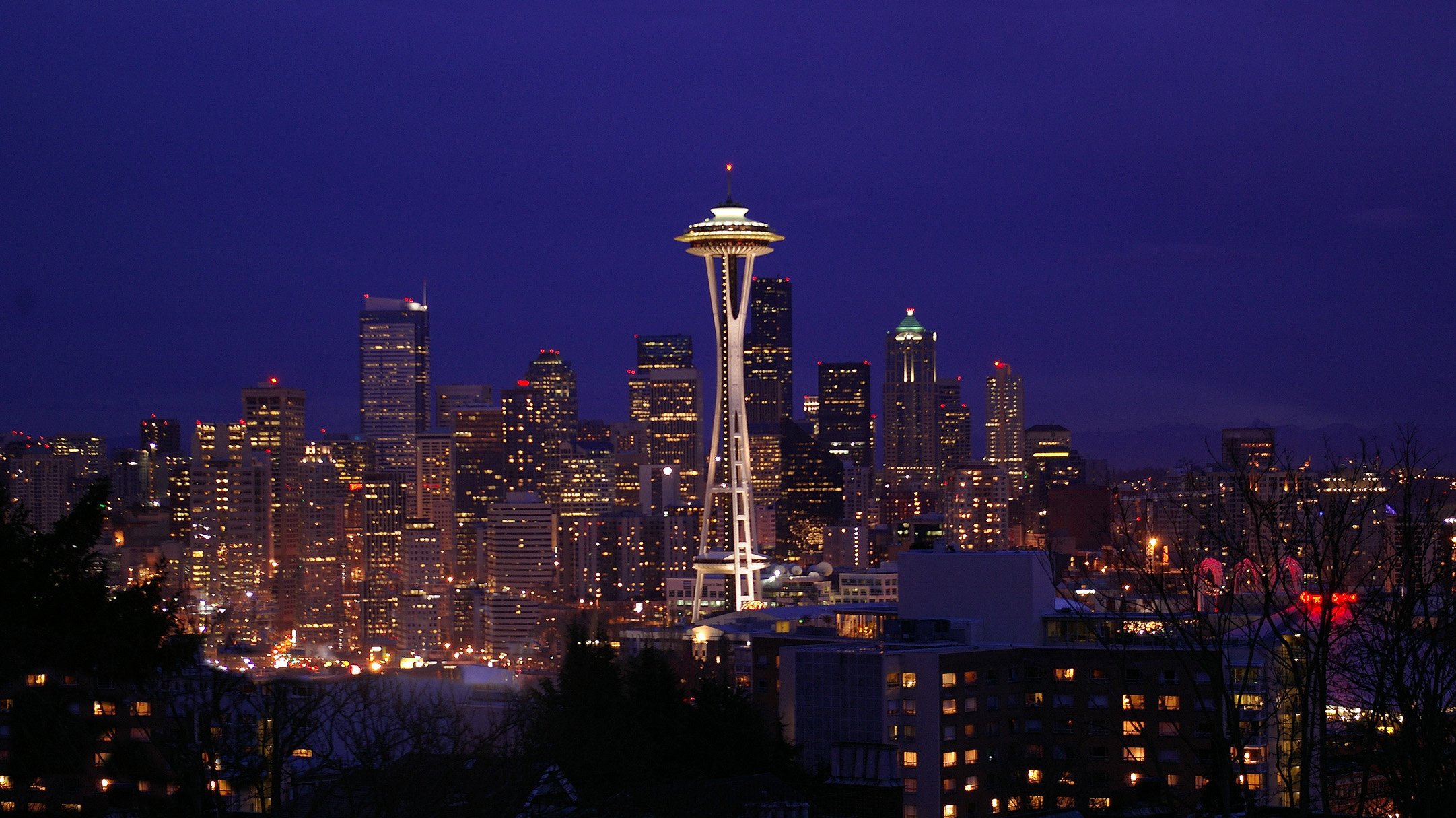 The illuminated Seattle skyline at night featuring the Space Needle and city skyscrapers against a dark blue sky.