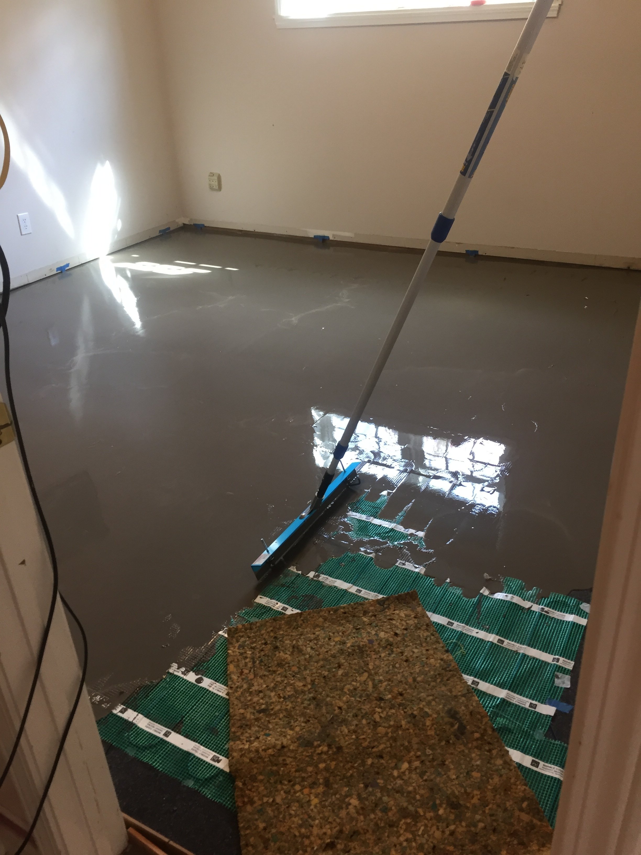 Self-leveling cement being spread over electric floor heating with a gauge rake