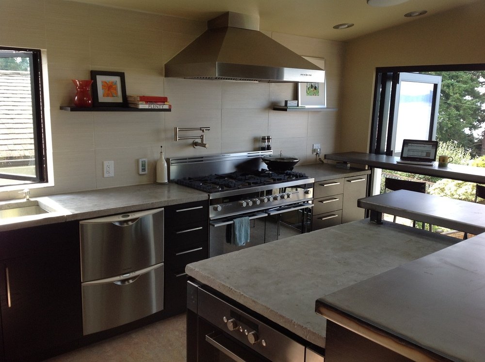 Modern residential kitchen featuring dark cabinetry, stainless steel appliances, and a concrete island countertop.