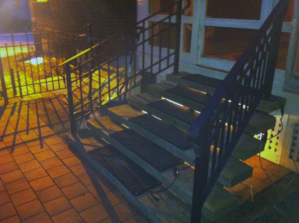 Black rubber snow melting stair mats installed on concrete steps with interconnected power cords for outdoor ice prevention.