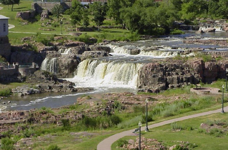 Cascading waterfalls of the Big Sioux River flowing over pinkish-red Sioux quartzite rock formations at Falls Park in Sioux Falls, South Dakota.