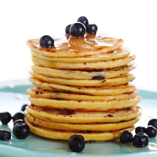A stack of golden-brown pancakes drizzled with syrup and topped with fresh blueberries on a teal plate in a breakfast nook.