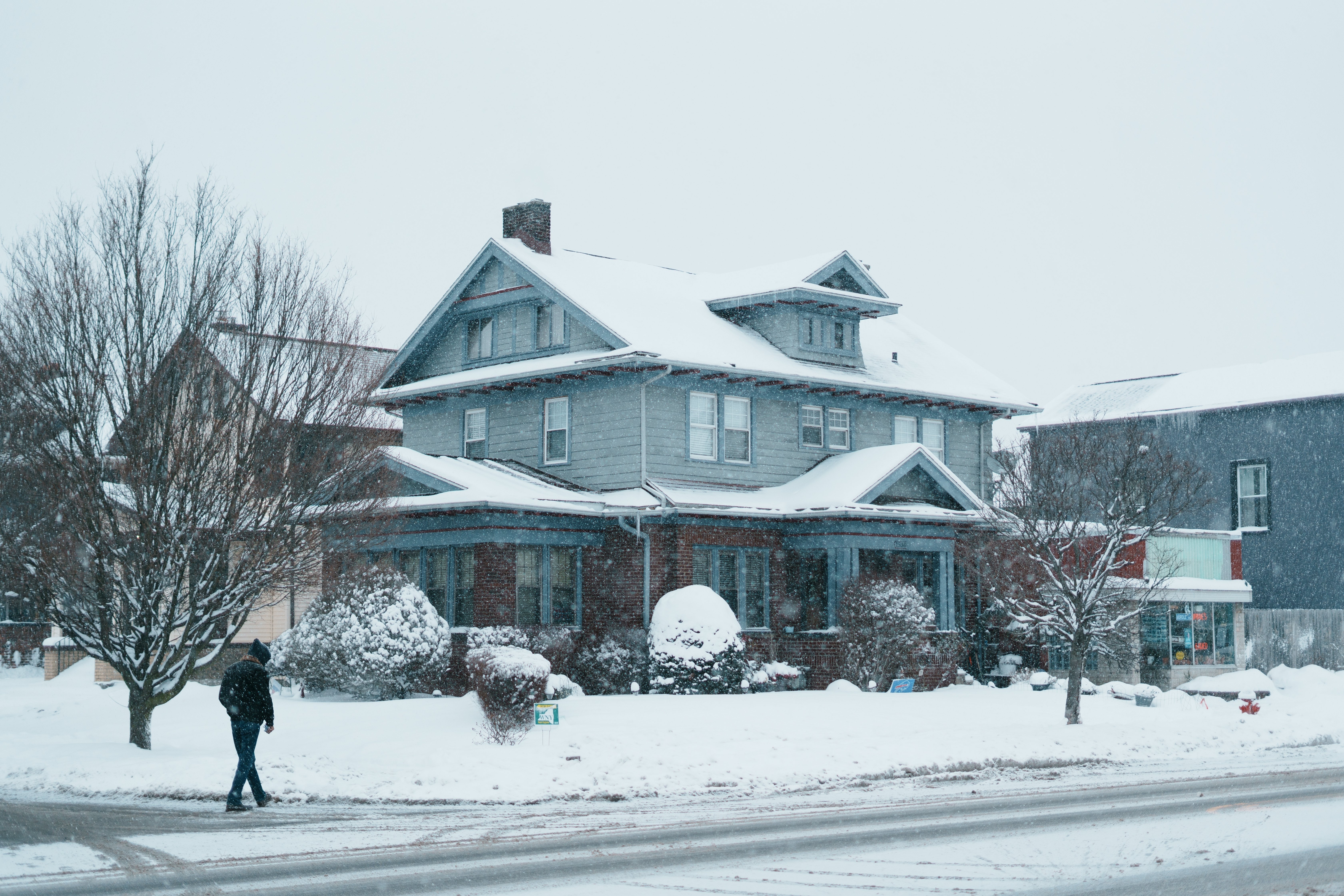 A two-story residential house in Buffalo, NY, covered in snow during a winter storm.