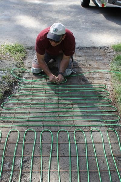 Contractor laying electric snow melting cables in sand base before paver installation for an accessible heated walkway.