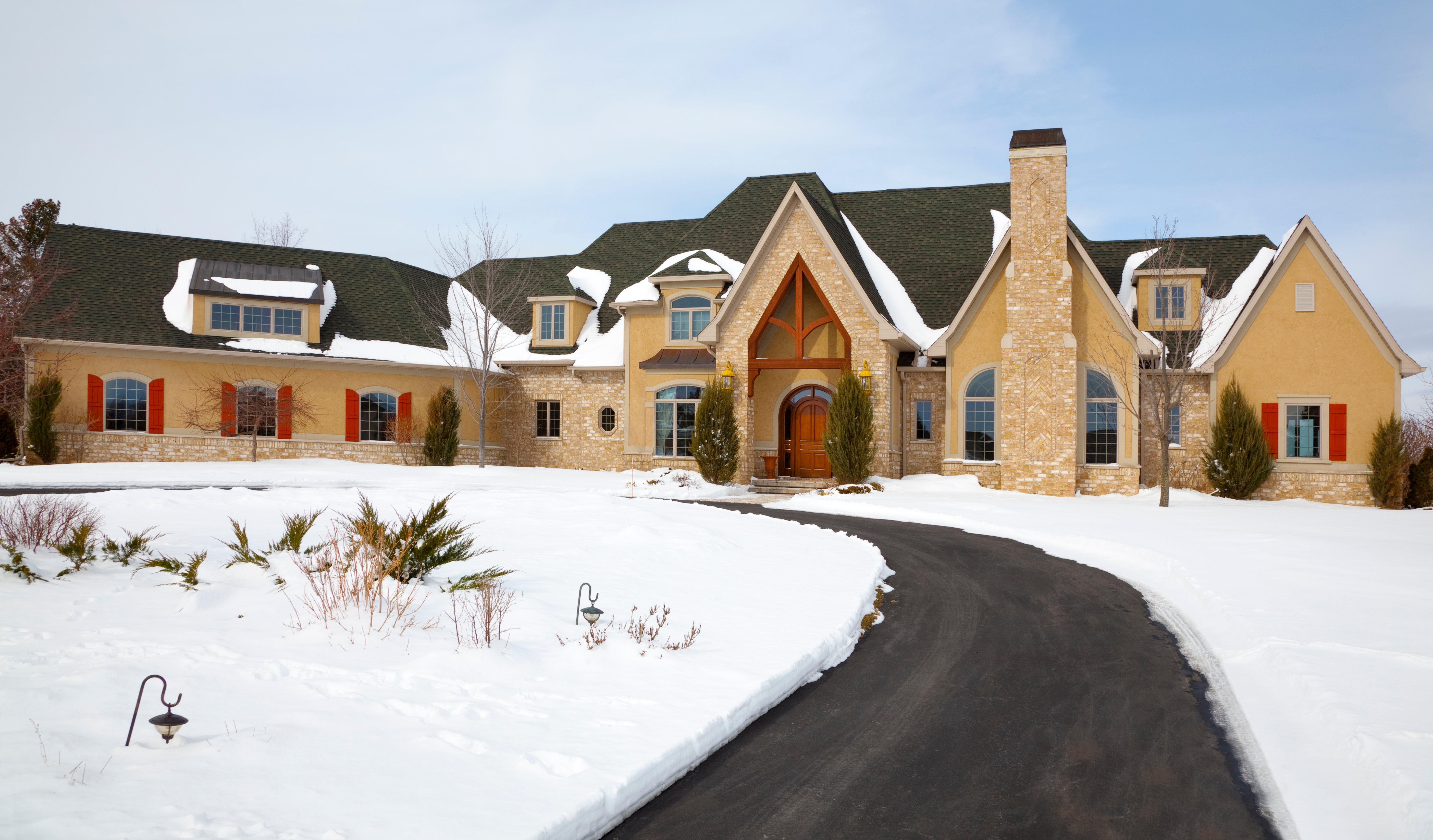 A snow melting system keeps a curved asphalt driveway clear of ice and snow in front of a stone and stucco residence during winter.