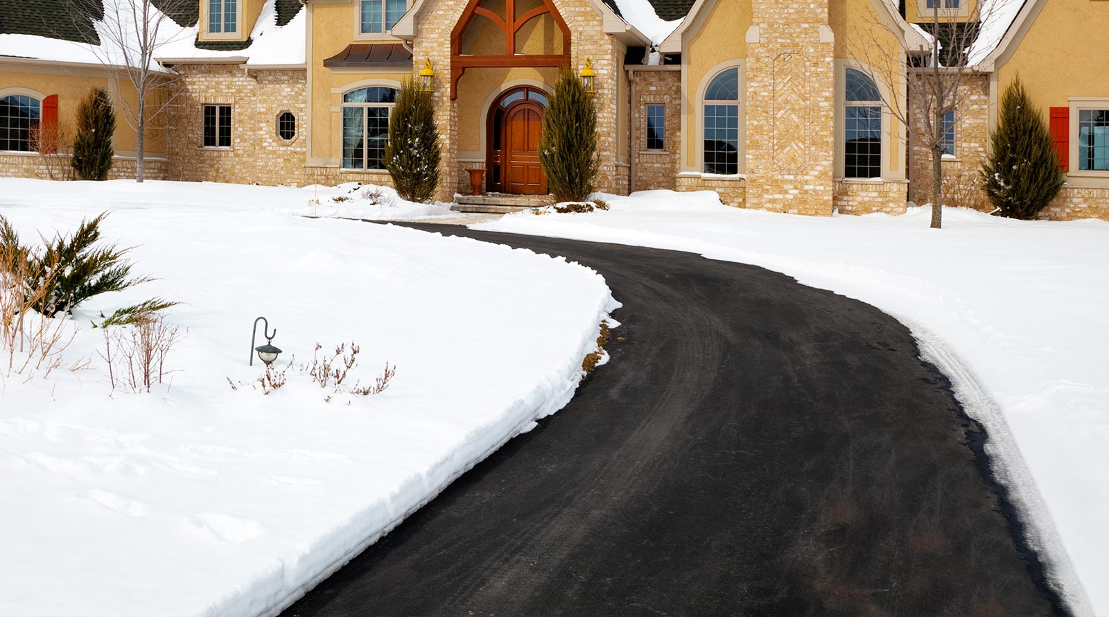 A clear asphalt driveway kept free of snow by an electric snow melting system in front of a residential home during winter.