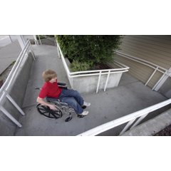 A young boy in a wheelchair on a concrete handicap-accessible ramp equipped with an integrated snow melting system.
