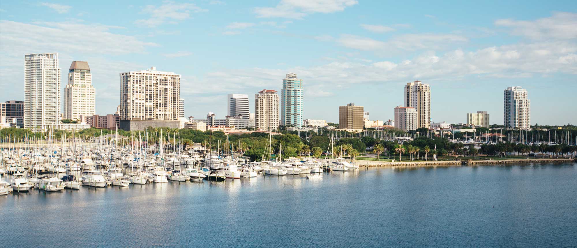 The skyline and waterfront marina of St. Petersburg, Florida, featuring docked boats and high-rise buildings under a clear blue sky.