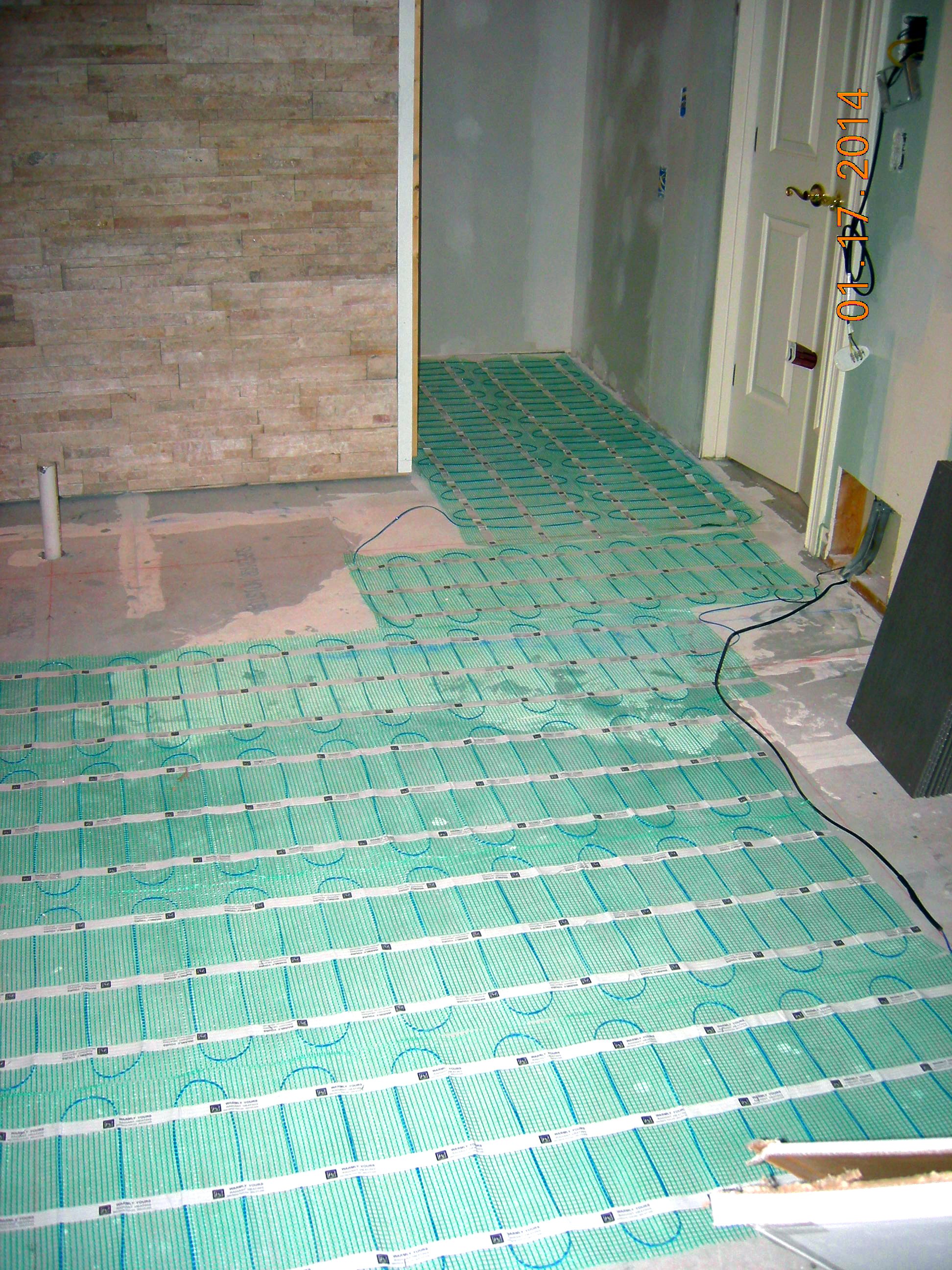 Bathroom floor showing green underfloor heating wire layout next to a tiled wall.