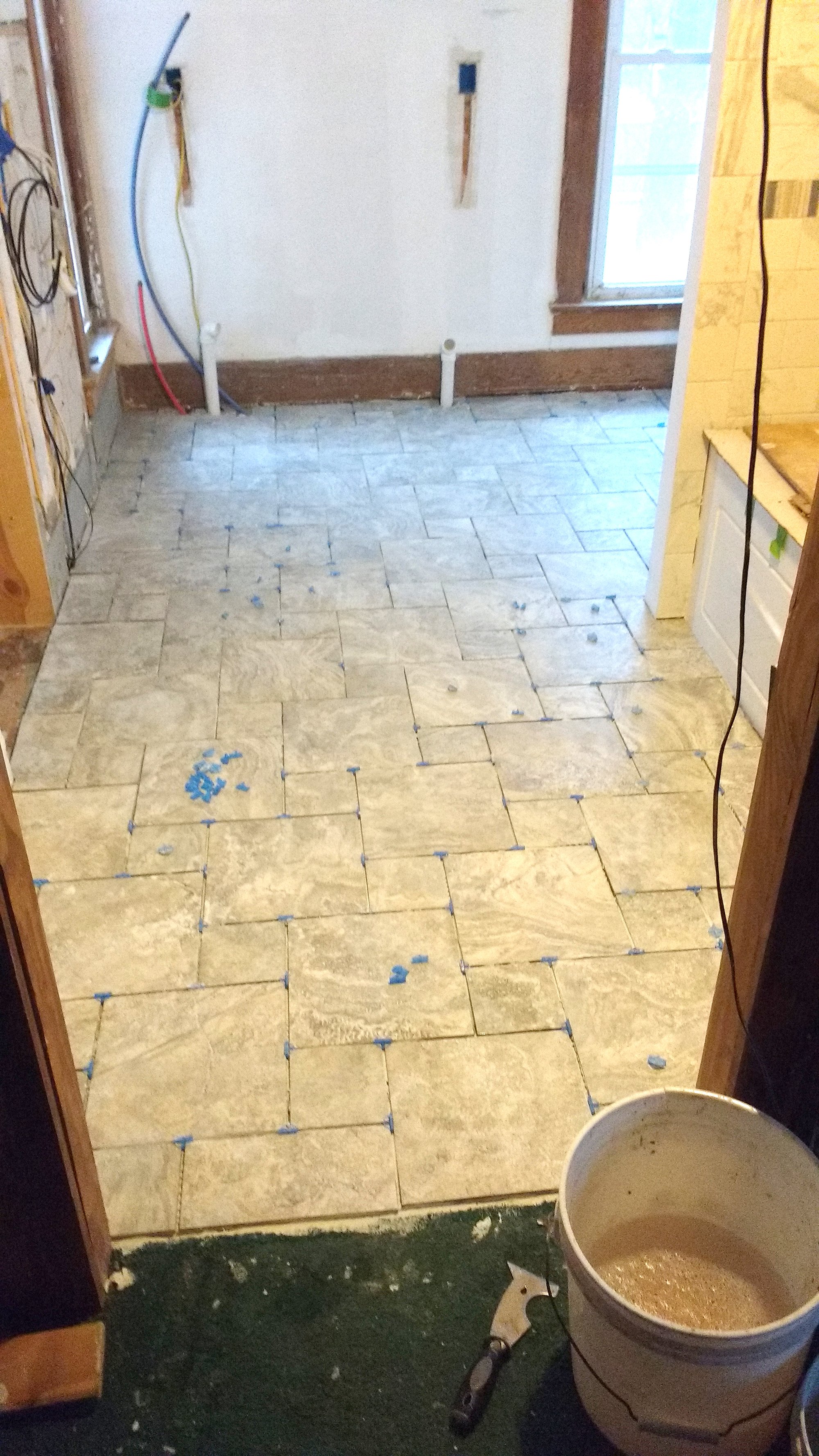 Newly laid tile floor with blue spacers during a bathroom renovation project.
